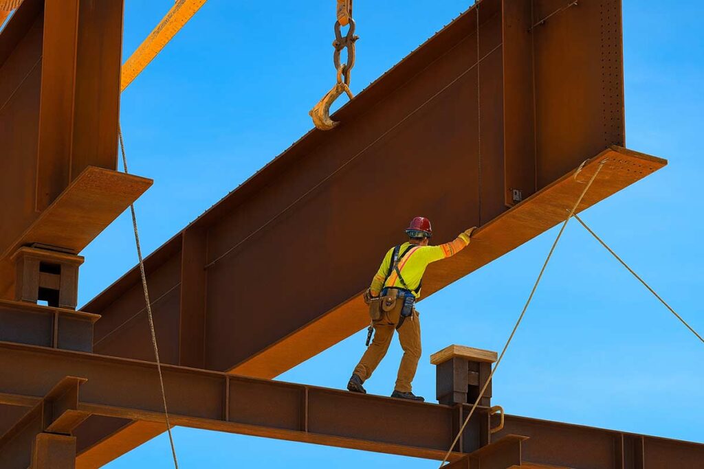 Ironworker guiding a suspended structural steel beam during installation.